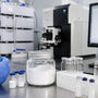 Researcher preparing powder sample vials beside chromatography instruments in a clean lab